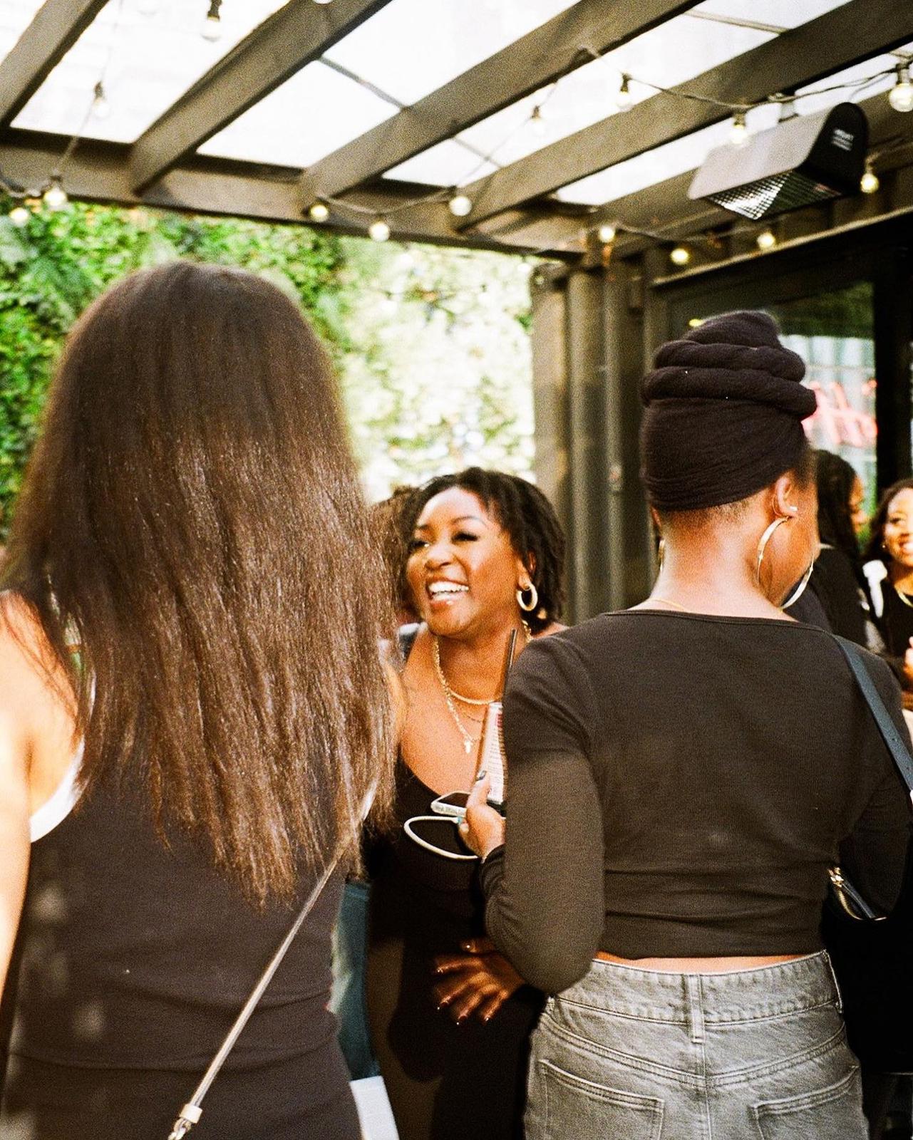 People socializing under a patio with string lights, focusing on two individuals' backs.